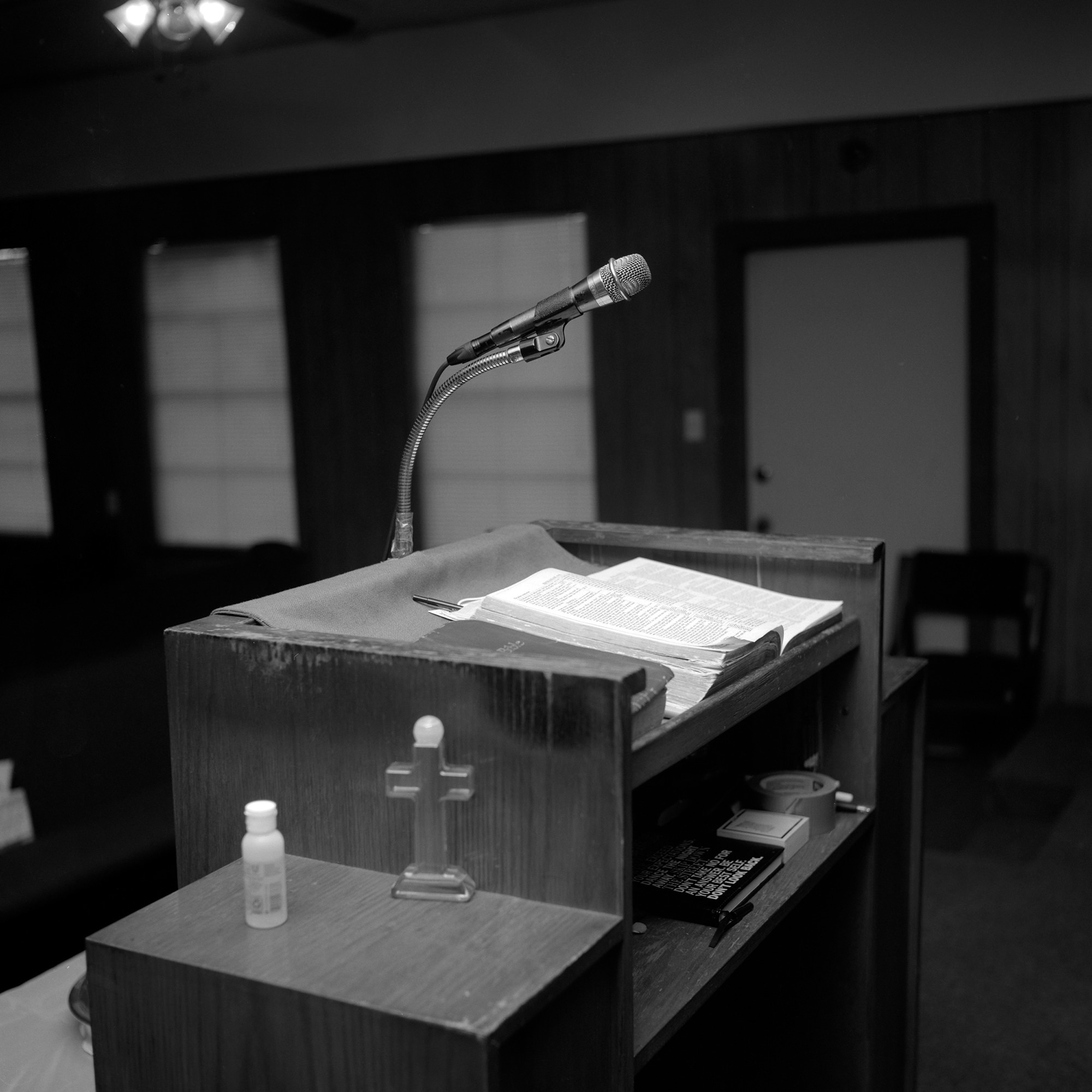 Image description: black-and-white photograph of church pulpit featuring a microphone, opened Bible. Art by Rahim Fortune.