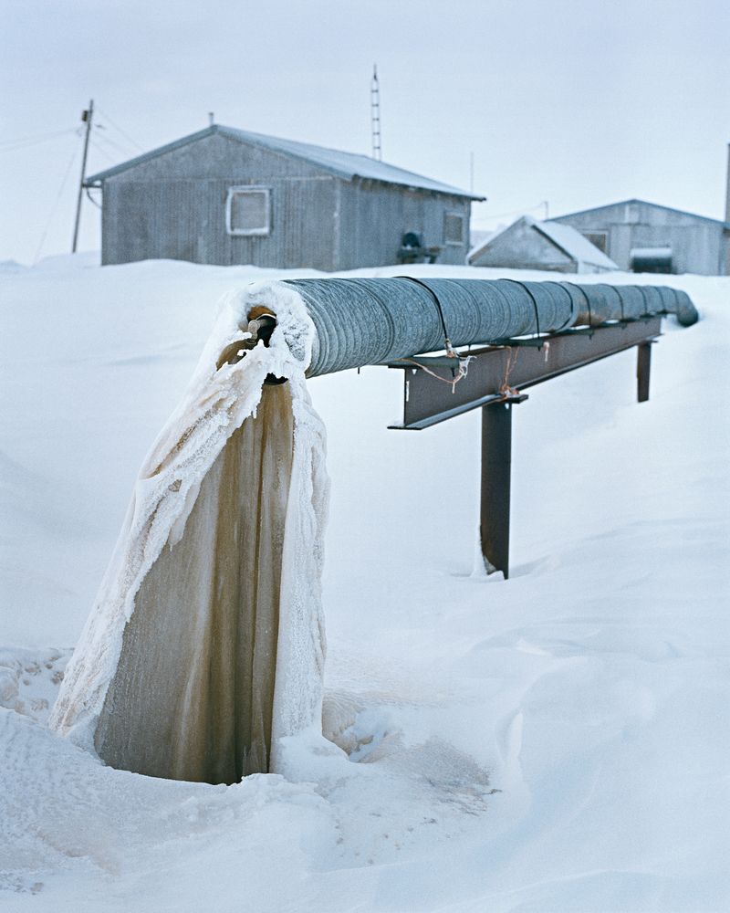 Frozen water hangs from a long pipe outside of a building.