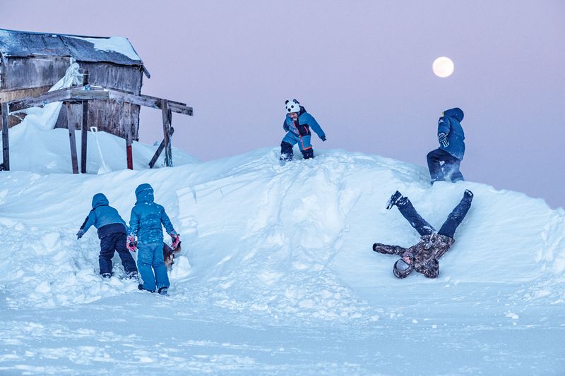 Five children and a dog play on a snowbank.