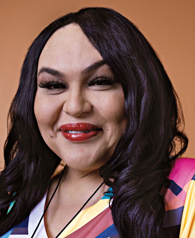 Headshot of a trans woman with long dark hair and bright red lipstick.