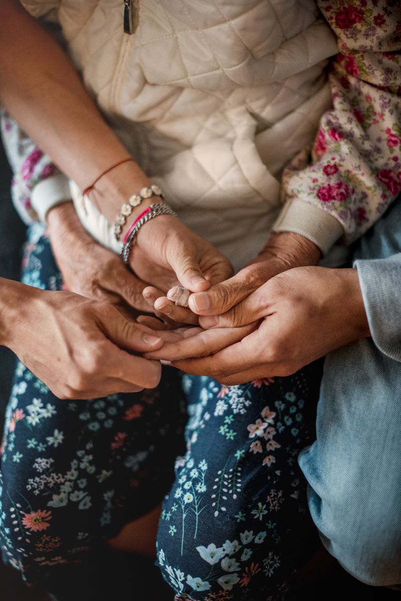 A close-up of three sets of hands from people of varying ages, holding hands together.