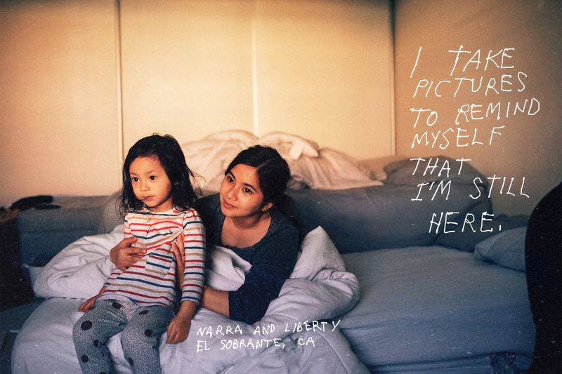 A woman holds a child on a couch. Over top of the photograph are the words, “I take pictures to remind myself that I’m still here. Marra and Liberty. El Sobrante, CA.”