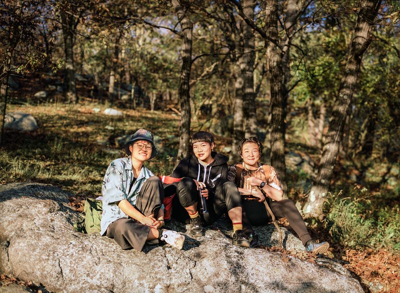 Tres personas en el bosque se sientan sobre una roca y sonríen a la cámara.