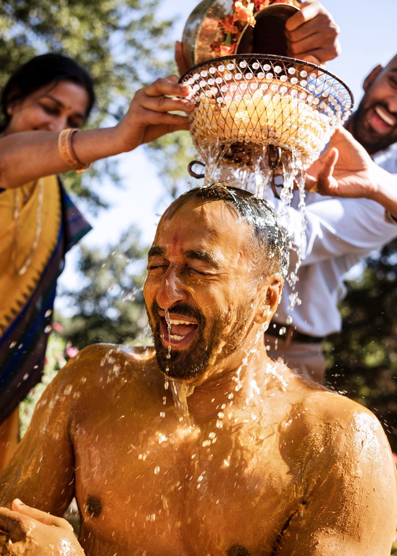 Two people pour water over a bare-chested man’s head.