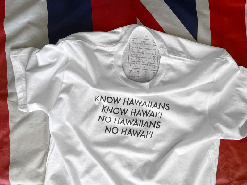 A white T-shirt with black letters reads, “Know Hawaiians. Know Hawai’i. No Hawaiians. No Hawai’i.”