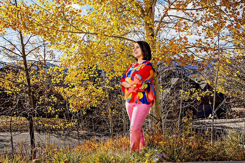 A woman stands with her arms crossed in front of a tree.