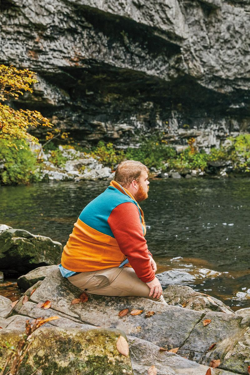 A man sits on a rock looking at the stream.