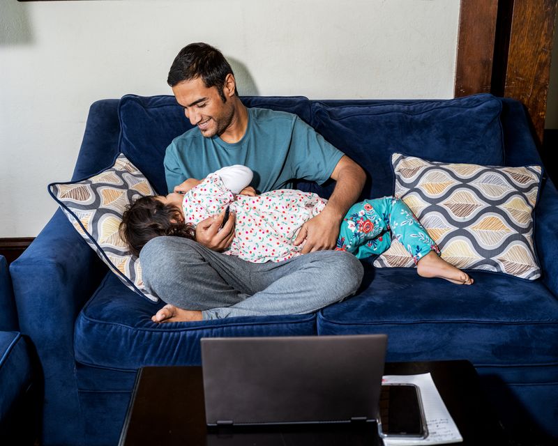 A man holds a young child on a blue couch.