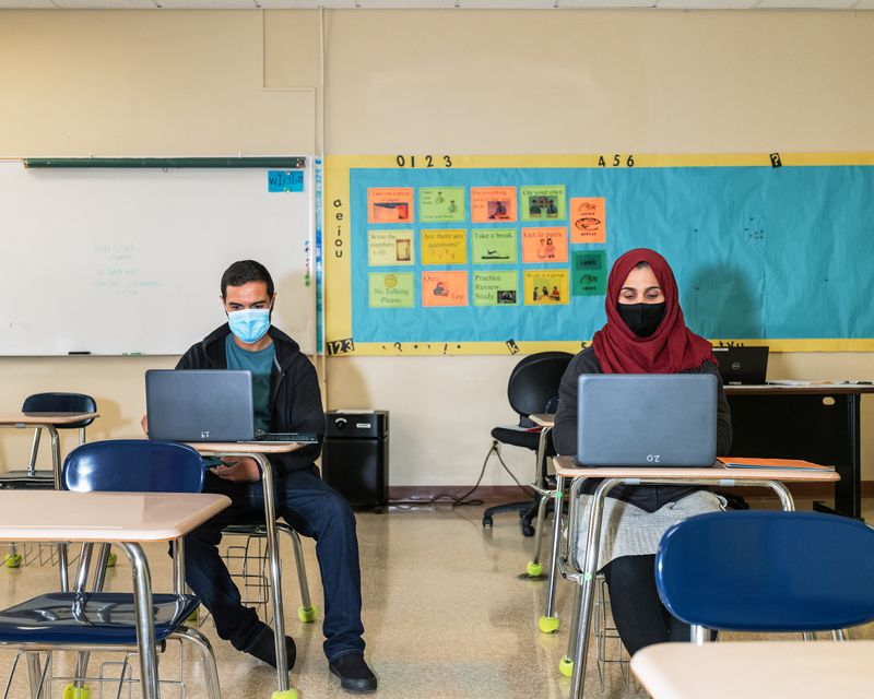 A woman and a man sit at desks in a classroom working on laptops.